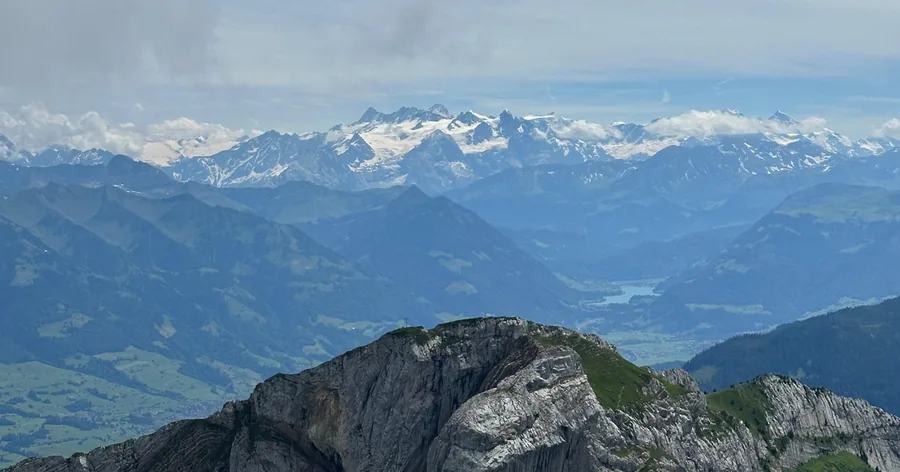 Blick vom Gipfel über Felsgrate zu den verschneiten Alpen