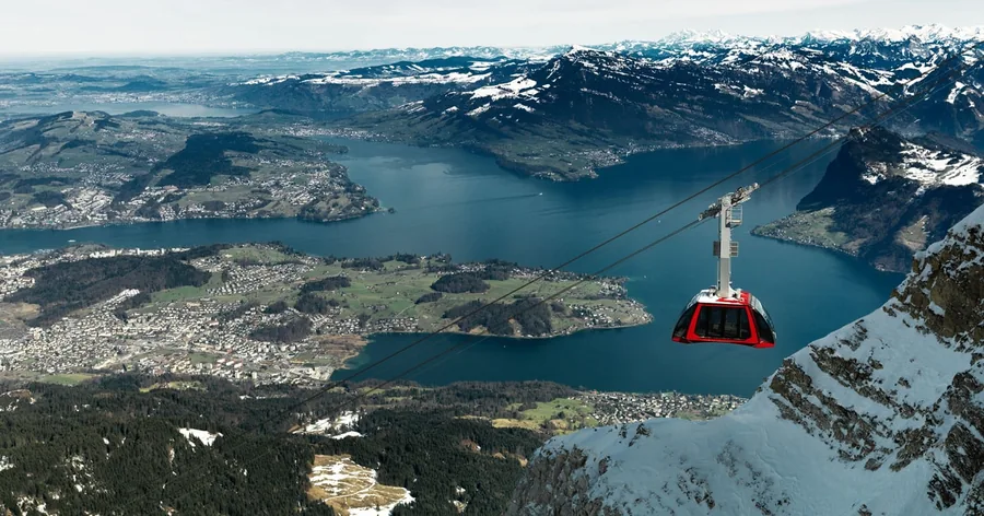 Eine rote Kabine der Luftseilbahn über dem See und der Stadt Luzern