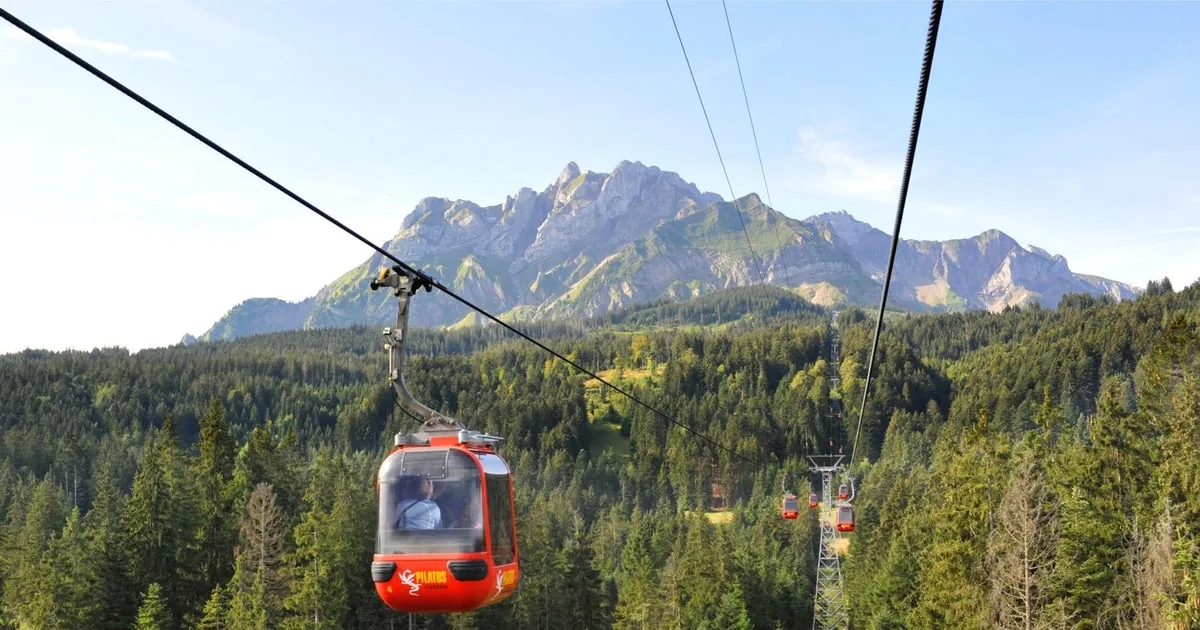 Eine rote Gondel über Fichtenwald, dahinter der felsige Grat des Pilatus
